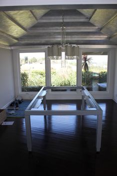 an empty room with a table and chairs in the center, near large open windows