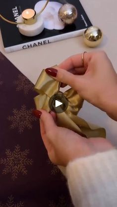 a person holding a gold bow on top of a table next to a book and candle