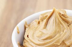 a white bowl filled with peanut butter on top of a wooden table