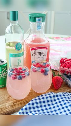 two glasses filled with pink lemonade and raspberries next to bottles of simply light