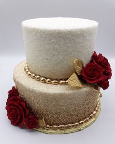 a three tiered cake with red roses on the bottom and gold trimmings