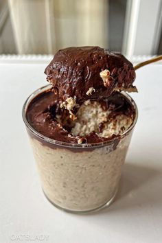 a spoon with some food in it on top of a glass cup that is filled with ice cream and chocolate