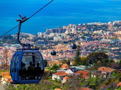 two people ride on a cable car above the city and ocean, with buildings in the background