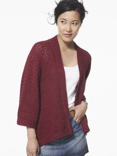 a woman standing in front of a white background wearing a red cardigan sweater and jeans