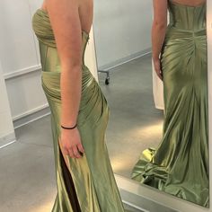 a woman in a green dress looking at herself in the mirror with her hand on her hip