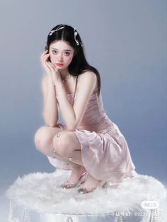 a woman in a pink dress is sitting on a white furnishing and posing for the camera