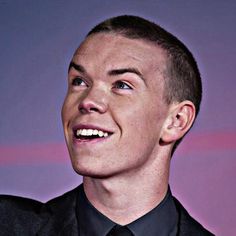 a young man wearing a black suit and tie smiling at something in the air above his head