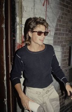 a woman in sunglasses is standing near a brick wall