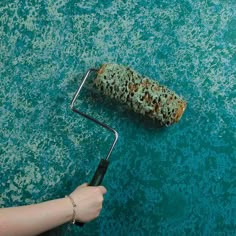 a hand holding a paint roller on top of a blue floor with green spots and rust