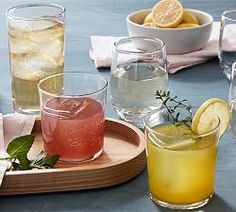 there are many different glasses on the table with lemons and water in them,