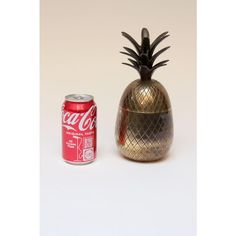 a small metal pineapple next to a can of coca - cola