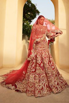 a woman in a red and gold bridal gown standing by an archway with her veil draped over her head