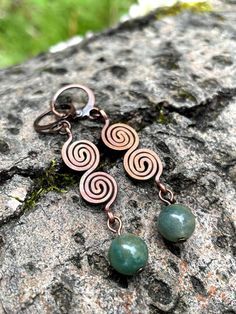 two copper and green earrings sitting on top of a rock