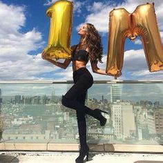 a woman holding two large gold balloons in front of her face with the letter m spelled out