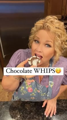 a woman eating a piece of chocolate while standing in front of a counter with the words chocolate whips on it