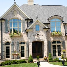 a large brick house with lots of windows and plants on the front door, along with landscaping