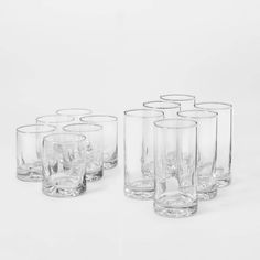 six clear glass tumblers are lined up on a white surface, one is empty