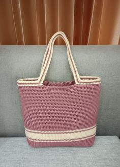 a pink and white bag sitting on top of a gray couch next to a window