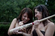 two young women are holding baseball bats and smiling at each other's faces as they laugh