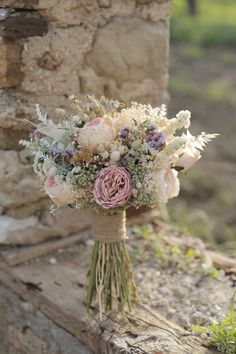 a bouquet of flowers sitting on top of a wooden bench next to a stone wall