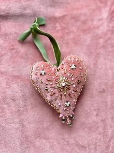 a pink heart shaped ornament hanging from a green ribbon on a pink cloth