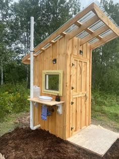 a small wooden outhouse with a sink and mirror on the outside, surrounded by mulch