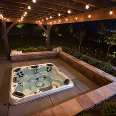 an outdoor hot tub in the middle of a patio with string lights strung around it