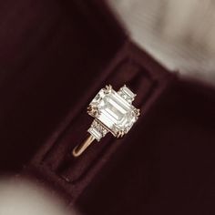 an engagement ring with three baguettes in it on a velvet box, close up