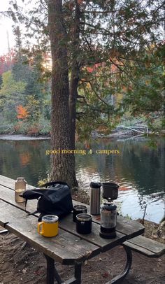 a picnic table with coffee cups on it next to a lake in the fall season