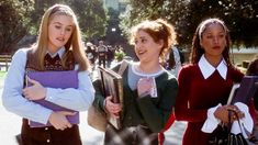 three girls in school uniforms are standing on the street and one girl is holding an accordion