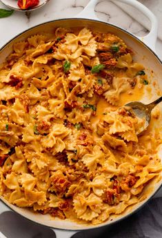 a skillet filled with pasta and sauce on top of a white marble countertop