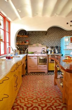 an old fashioned kitchen with yellow cabinets and pink stove top oven in the center of the room