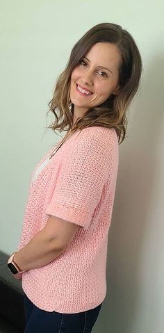 a woman standing in front of a white wall wearing a pink sweater and blue jeans