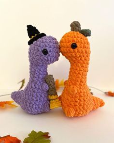 two crocheted stuffed animals sitting next to each other on a white surface with autumn leaves around them