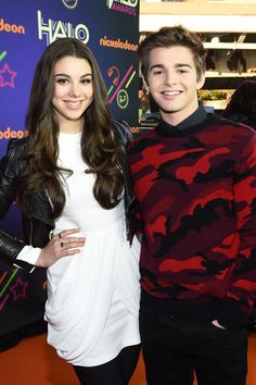 two people standing next to each other on a red and black carpeted area with neon signs in the background