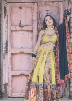 a woman standing in front of a wooden door wearing a yellow and black lehenga