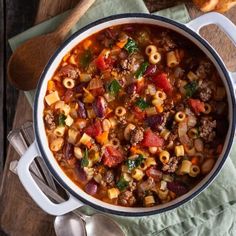 a large pot filled with pasta and meat soup on top of a wooden cutting board