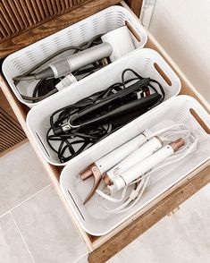 two white baskets filled with hairdryers on top of a wooden dresser next to a drawer