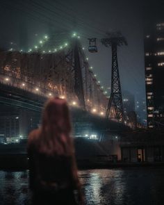 a woman standing in front of a bridge at night with the city lights shining on it