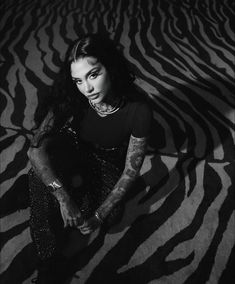 a woman sitting on top of a zebra print floor next to a wall with tattoos