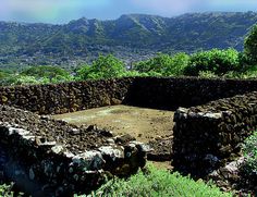 a stone structure in the middle of a field with trees and mountains in the background