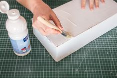 someone using a brush to paint the inside of a box with glue and paper on it