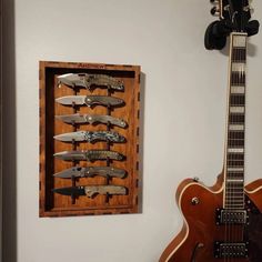 a guitar is hanging on the wall next to a wooden case with knives in it