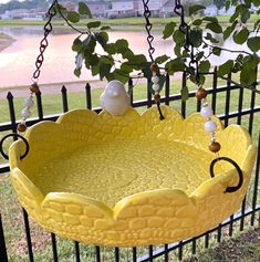 a yellow bird bath sitting on top of a metal fence next to a tree branch