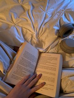 a person is reading a book while laying in bed with headphones on their ears