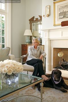 a woman sitting in a chair next to a dog on the floor near a fireplace