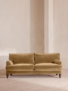 a tan couch sitting on top of a hard wood floor next to a white wall