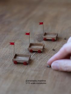 a person's hand is pointing at small wooden cars with red flags on them