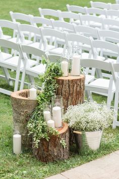 wedding ceremony decor with candles and greenery on tree stumps in front of white chairs