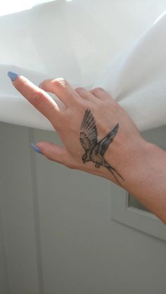 a woman's hand with a bird tattoo on her left wrist and blue nail polish